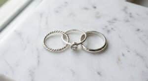 Three 925 sterling silver rings on white marble — polished band, CZ accent ring, and twisted rope design