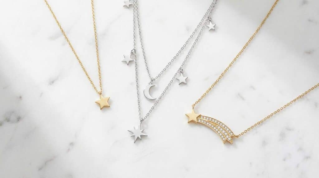 Types of star necklaces flat lay including dainty gold star pendant, layered silver star set, and shooting star necklace on white marble